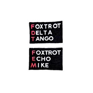 May include: Two black fabric patches with white letters and red outlines. The top patch says "FOXTROT DELTA TANGO" and the bottom patch says "FOXTROT ECHO MIKE".