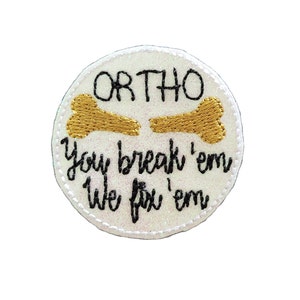 May include: White round embroidered patch with the text "ORTHO You break 'em We fix 'em" and a gold embroidered bone.