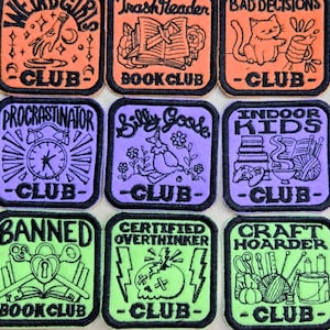 May include: Nine embroidered patches with black borders. The patches feature various designs and text, including "Weird Girls Club," "Trash Reader Book Club," and "Bad Decisions Club." Other patches say "Procrastinator Club," "Silly Goose Club," and "Indoor Kids Club."
