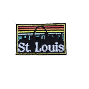 May include: Embroidered patch with a black silhouette of the St. Louis skyline, including the Gateway Arch, against a colorful sunset background. The text "St. Louis" is embroidered in white below the skyline.