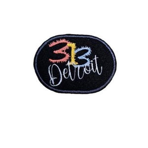 May include: Black oval embroidered patch with the text "313 Detroit" in white, with the numbers "313" in pink, yellow, and blue.