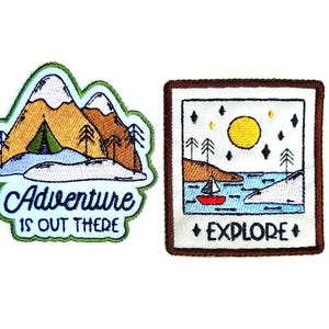 May include: Two embroidered patches. One features mountains, a tent, and the text "Adventure is Out There." The other depicts a sailboat on water under a sun and stars, with the word "Explore."