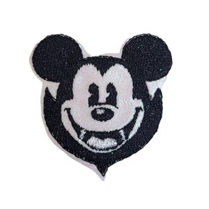 May include: A white and black embroidered iron-on patch of Mickey Mouse with fangs. The patch has a glittery background.