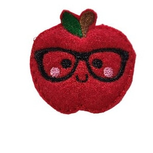 May include: Red felt apple with a smiling face, wearing black-rimmed glasses. The apple has a green stem and leaf.