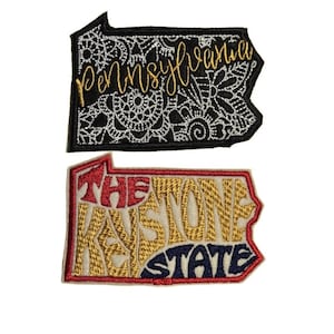 May include: Two embroidered patches in the shape of the state of Pennsylvania. The top patch is black with white and silver embroidery that reads "Pennsylvania". The bottom patch is white with red, gold, and blue embroidery that reads "The Keystone State".