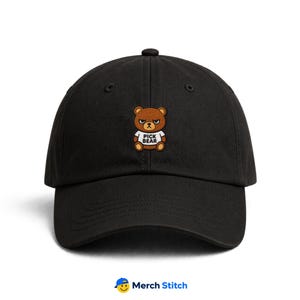 May include: A black baseball cap featuring an embroidered brown bear character wearing a white t-shirt with the text PICK BEAR printed in black. The cap has a structured crown, a curved brim, and a button on top, presenting a clean design.