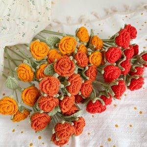 May include: A bouquet of crocheted roses in shades of orange and red. The roses are arranged in a circular pattern and have green leaves.
