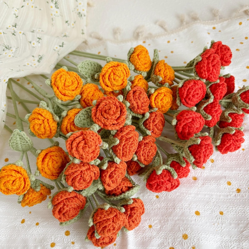 May include: A bouquet of crocheted roses in shades of orange and red. The roses are arranged in a circular pattern and have green leaves.
