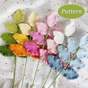 May include: A collection of crochet leaf stems in various colors, including green, yellow, orange, pink, and blue. Each leaf is intricately crocheted with detailed veining. The stems are a light green color. The word "Pattern" is in a green oval.