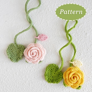 May include: Crocheted floral design featuring a pink and yellow rose, green leaves, and stems. The word "Pattern" is in a green oval. The flowers are handmade and appear to be attached to a white surface.