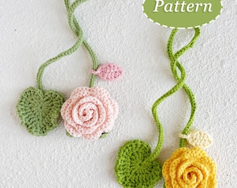 May include: Crocheted floral design featuring a pink and yellow rose, green leaves, and stems. The word "Pattern" is in a green oval. The flowers are handmade and appear to be attached to a white surface.