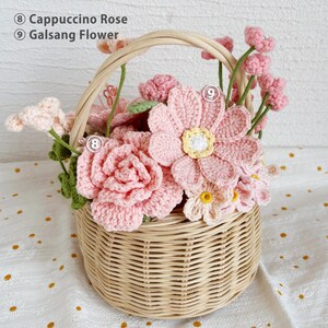 May include: A wicker basket filled with crocheted flowers in shades of pink. The flowers include a cappuccino rose and a galsang flower.