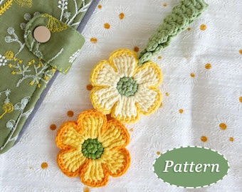 May include: Two crochet flower appliques in yellow and orange with green centers, and a green crochet strap. A green floral patterned fabric with a button is visible in the background. The word "Pattern" is in a green oval.