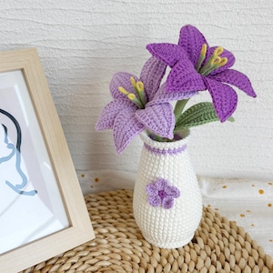Puede incluir: Un jarrón de ganchillo con un diseño de flores moradas y un ramo de lirios de ganchillo morados.