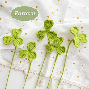 May include: Five crocheted green shamrock leaves with stems on a white background with a small yellow floral pattern. The text "Pattern" is written in green on a light green oval.