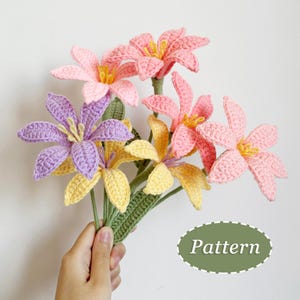 Op de afbeelding: Een boeket handgemaakte haakbloemen in roze, geel en paars. De bloemen hebben gedetailleerde bloemblaadjes en gele centra. De stelen zijn groen en de tekst "Pattern" is zichtbaar.