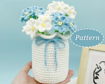 May include: A crocheted vase with a blue ribbon and a bouquet of white and blue flowers. The vase is white and the flowers are made of yarn. The word "Pattern" is written in a circle on the right side of the image.