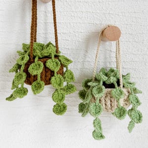 May include: Two crocheted hanging plant pots with green leaves. The pot on the left is brown and the pot on the right is beige.