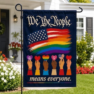 May include: A dark blue garden flag featuring the text We The People means everyone. The design includes a brushstroke-style American flag transitioning into a rainbow flag above six hands holding heart-shaped icons with various symbols.