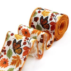 May include: A roll of white textured ribbon with a repeating pattern of orange monarch butterflies, red berries, brown acorns, and autumn leaves in shades of yellow, orange, and green. The edges of the ribbon are finished with orange stitching.
