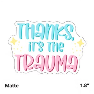 Puede incluir: Adhesivo mate con el texto "Thanks, it's the Trauma" en azul y rosa, delineado en blanco. El adhesivo mide 4,57 cm y tiene un borde blanco con detalles de estrellas amarillas.