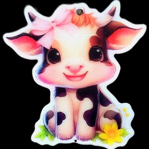 Pode incluir: Uma vaca de desenho animado fofa com um laço rosa, manchas pretas e brancas e um rosto sorridente. A vaca está sentada em um pedaço de grama verde com uma flor amarela. A imagem tem um efeito brilhante.