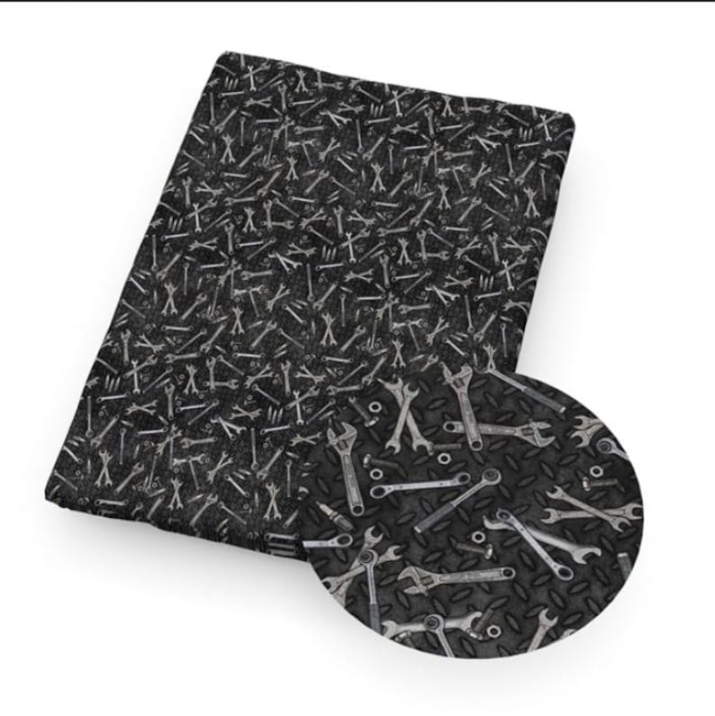 May include: A rectangular piece of fabric featuring a repeating pattern of various silver-colored metal wrenches and small hardware nuts scattered across a dark black background with a textured diamond plate metal pattern throughout the design.