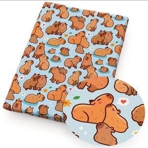 May include: A folded fabric featuring a repeating pattern of cartoon capybaras in various poses on a light blue background. The capybaras are shades of brown and tan, with some holding leaves or flowers. A circular inset shows a close-up of the pattern.