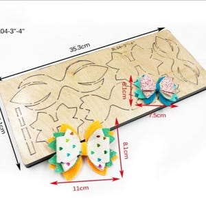 May include: A wooden die-cut template for making decorative bows, measuring 13.9 inches long and 5.9 inches wide. Two finished bows are displayed, one yellow and the other blue, each with a unique design. The template is labeled "BL04-3"-4".