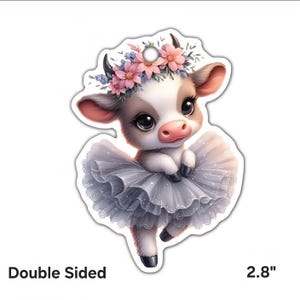 Pode incluir: Enfeite de dupla face, recortado, com uma bezerra de desenho animado em um tutu e coroa de flores. A bezerra é branca e marrom com olhos grandes e nariz rosa. O tutu é cinza e as flores são rosa e azuis. O enfeite tem 7,1 cm.