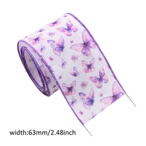 May include: A roll of white ribbon featuring a repeating pattern of purple and pink butterflies with purple stitched edges. The ribbon has a width of 63mm as indicated by the text printed at the bottom of the image.