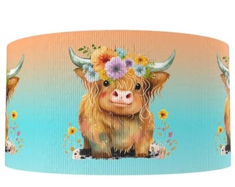 May include: A cylindrical lampshade featuring a repeating pattern of a Highland cow wearing a floral crown. The cow has long, shaggy brown fur, a pink nose, and large horns. The background transitions from orange to blue.