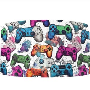 May include: A white background with a repeating pattern of colorful video game controllers. The controllers are in various shades of blue, green, pink, orange, and purple. The controllers are surrounded by white paint splatters.
