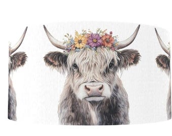 May include: A watercolor illustration of a Highland cow wearing a floral crown. The cow has long, shaggy brown fur and large horns. The floral crown features a variety of colorful flowers. The background is white.