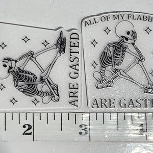 Puede incluir: Dos pegatinas rectangulares transparentes con un diseño de esqueleto. Un esqueleto está acostado, el otro está sentado. Ambas pegatinas tienen el texto "ALL OF MY FLABBERS ARE GASTED" y miden aproximadamente 5 cm de largo.