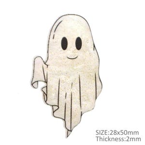 May include: A glittery white ghost-shaped decoration with black eyes and a smiling mouth. The ghost has a flowing sheet design and is 28x50mm in size with a 2mm thickness. The image includes the text "SIZE: 28x50mm Thickness: 2mm".