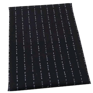 May include: Black wrapping paper with a repeating pattern of the words "FUCK YOU" in white, arranged in vertical columns. The paper is slightly angled, showing its folded edges.