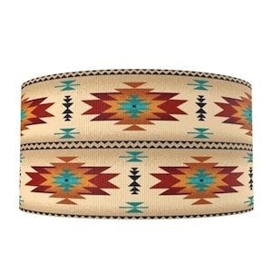 May include: A cylindrical lampshade with a Southwestern pattern. The design features repeating geometric shapes in shades of red, orange, turquoise, and black against a beige background. The edges are trimmed with a zigzag pattern.