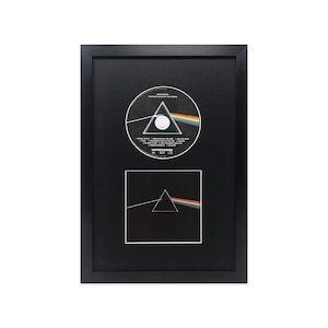 May include: A black framed display featuring a CD and a print of the album cover for Pink Floyd's "The Dark Side of the Moon". The CD showcases the album's iconic prism design and the tracklist. The print is a black and white image of the prism.