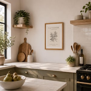 May include: A framed wall print titled LA CUISINE with a botanical illustration of herbs, centred on a kitchen wall. The print features black text on a cream background, housed in a light wood frame, positioned above olive green cabinets.