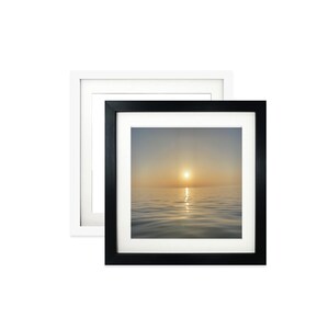 May include: Two framed art prints. One in a black frame, the other in white. The art is a photograph of a sunset over water. The sun is a bright yellow orb, reflecting on the water's surface.