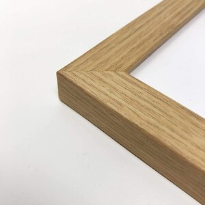 May include: Close-up of a corner of a natural wood picture frame. The frame is a light brown color with a smooth finish.