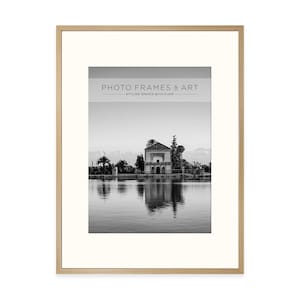 May include: A framed black and white photograph of a building reflected in water. The frame is light brown, and the mount is off-white. The text "PHOTO FRAMES & ART" is at the top of the image.