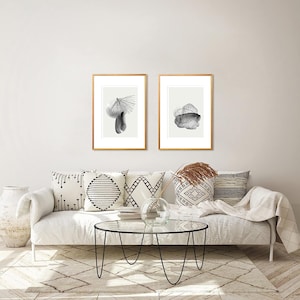 May include: Two black and white abstract art prints in gold frames are hung above a white couch with throw pillows. The couch is in a living room with a glass coffee table and a rug.