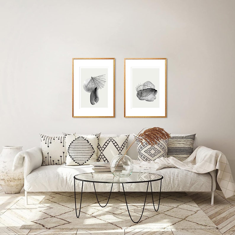 May include: Two black and white abstract art prints in gold frames are hung above a white couch with throw pillows. The couch is in a living room with a glass coffee table and a rug.
