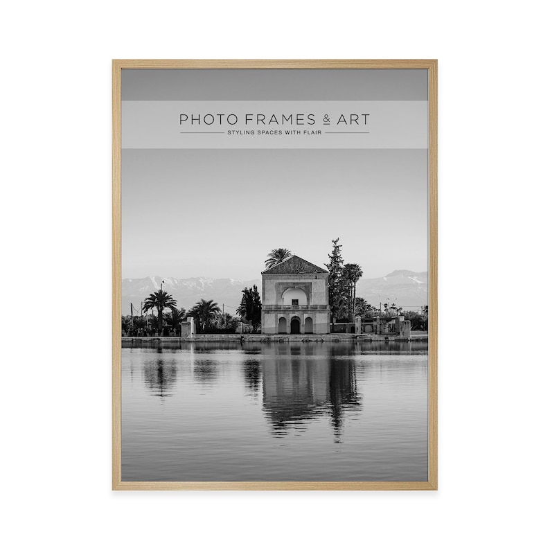 May include: Black and white framed print featuring a serene landscape with a building reflected in calm water. The print is in a light wood frame. Text at the top reads "PHOTO FRAMES & ART" and "STYLING SPACES WITH FLAIR".