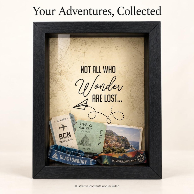 May include: A black shadow box frame containing a beige background with the text "Your Adventures, Collected" and "NOT ALL WHO Wonder ARE LOST..." with a paper airplane graphic. Inside are various travel tickets and two fabric wristbands.