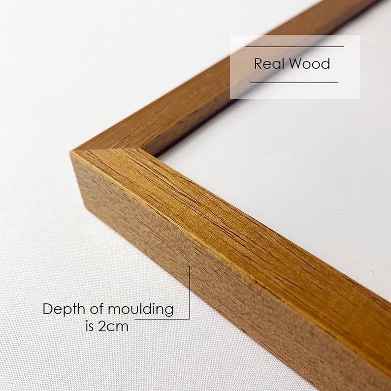 May include: Close-up of a wooden picture frame with a natural wood finish. The frame is 2 inches deep and has a beveled edge. The text "Real Wood" is printed on the frame.