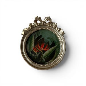 May include: A silver-coloured, oval picture frame with a bow detail at the top. Inside the frame is a circular painting of a bird of paradise flower with red and orange petals and green leaves on a dark green backdrop.