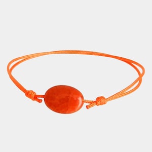 Puede incluir: Pulsera naranja brillante con una gema ovalada y pulida en el centro. La pulsera está hecha con un cordón naranja fino, anudado a cada lado de la gema. El cordón es ajustable.